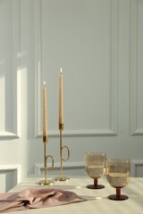 Glasses of wine near burning candles on white table indoors