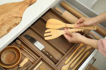 Woman taking wooden spatula and fork from open drawer of kitchen cabinet, above view - obrazy, fototapety, plakaty