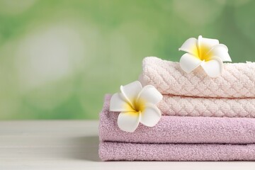 Fototapeta na wymiar Closeup view of soft folded towels and plumeria flowers on white wooden table, space for text