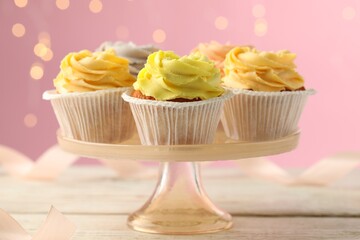 Stand with tasty cupcakes on white wooden table against blurred lights