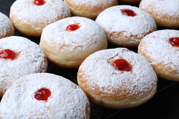 Fototapeta na wymiar Many delicious donuts with jelly and powdered sugar on cooling rack, closeup