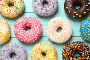 Delicious glazed donuts on blue wooden table, flat lay