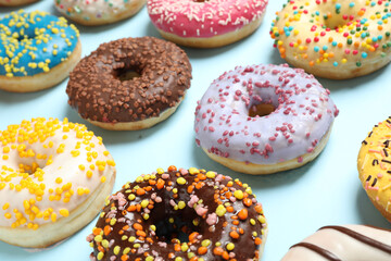 Delicious glazed donuts on light blue background, closeup