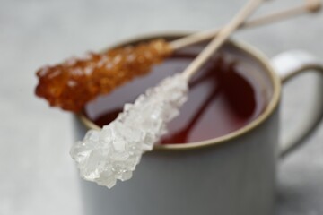 Sticks with sugar crystals and cup of tea on table, closeup