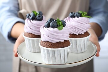 Woman holding plate with sweet cupcakes, closeup