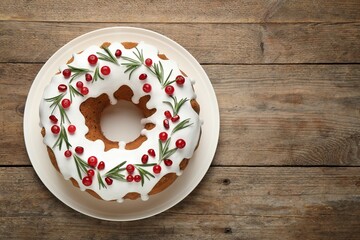 Traditional Christmas cake decorated with glaze, pomegranate seeds, cranberries and rosemary on wooden table, top view. Space for text