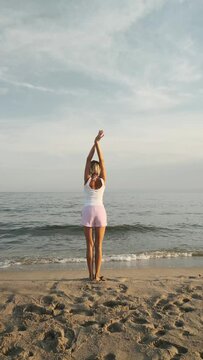 Back view of a woman stretching and relaxing on the sea shore at the beach. Freedom, mindfulness and meditation concept.