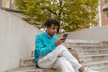 Obraz premium Dark-skinned man looking at smartphone sitting on steps