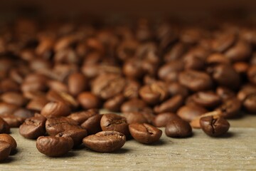 Many roasted coffee beans on wooden table, closeup