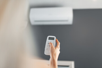 Young blonde female holds remote control of the air conditioner.