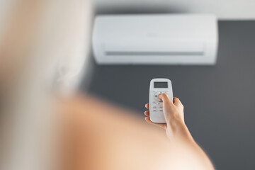 Fototapeta Young blonde female holds remote control of the air conditioner. obraz