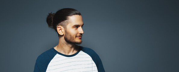 Portrait of attractive young man with beard and long dark hair, looking away.