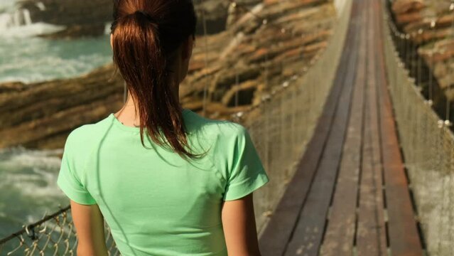 Sporty woman running on mountain road in beautiful nature. A brunette runner woman runs in the park jogging. sports girl back view runs in the morning on a suspension bridge near the ocean, america