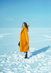 Fototapeta Young stylish woman in yellow coat walking on snowy ice.  obraz