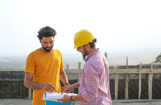 Two pakistani or indian workers, standing and looking at map file, construction site photography