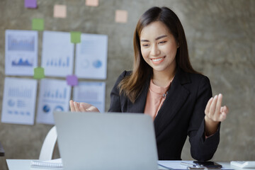 Beautiful Asian businesswoman sitting in her private office, she is talking to her partner via video call on her laptop, she is a female executive of a startup company. Concept of financial management