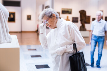 mature woman examines sculpture in an exhibition in hall of an art museum