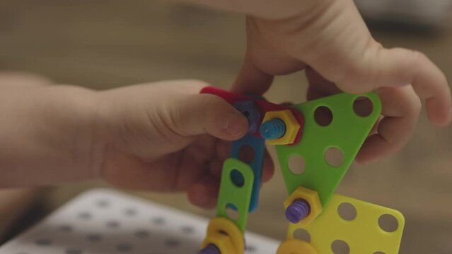 baby child hands screwing nut and screw-bolt plastic game set constructor puzzle. close-up view kid's fingers playing colorful nuts screws, making building form. concept developing fine motor skills