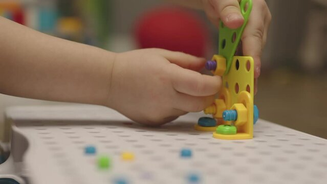 baby child hands screwing nut and screw-bolt plastic game set constructor puzzle. close-up view kid's fingers playing colorful nuts screws, making building form. concept developing fine motor skills