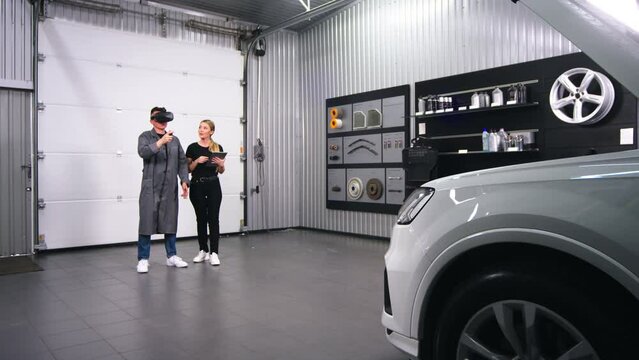 mechanics, a man and a woman, in a car service check and inspect the car together during diagnostics in virtual reality headsets. The concept of modern diagnostics and new technologies for car repair.