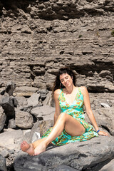 brunette woman sitting on some rocks with a green dress