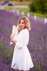 Fototapeta na wymiar Young woman in a white dress and straw hat running in a lavender field 
