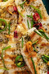 Macro close-up of grilled chicken breast cooked with three different colors chili peppers and aromatic herbs.