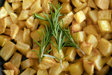 Macro close-up of a rosemary sprig with homemade baked potatoes on the background.