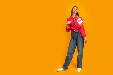 Naklejka premium Full-length young woman holds the flag of Canada. Bright yellow background. Study in Canada. Space for text