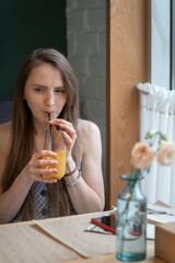 Young woman in cafe drinks cocktail juice beverage through straw. Girl relaxes at table in cafe. Vertical frame.