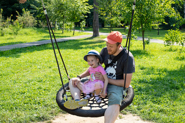 Caucasian girl 4 years old swinging on a nest swing, family vacation with parents, dad with daughter