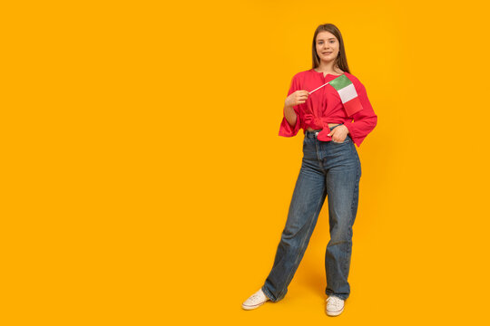 Full-length portrait of young girl with the flag of Italy on orange background. Learn Italian. Immigration to Italy. Copy space.
