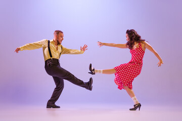 Beautiful girl and man in colorful retro style costumes dancing incendiary dances isolated on lilac color background in neon light. Concept of art, culture