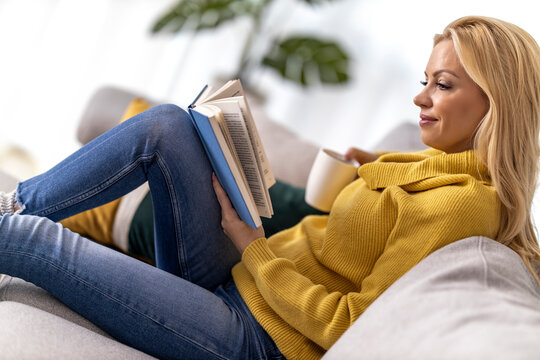 Woman drinking coffee and reading book at home