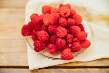 Raspberry fruits on a small saucer, a bunch of summer berries on a wooden background. Summer background. Juicy appetizer or dessert.