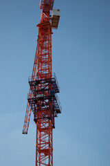 A red orange construction tall crane against a clear blue blue sky in the sunshine of the day in the rays of the sun. Construction site on the background blue sky, panoramic mock-up