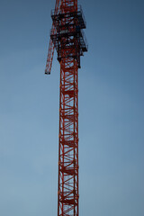 A red orange construction tall crane against a clear blue blue sky in the sunshine of the day in the rays of the sun. Construction site on the background blue sky, panoramic mock-up