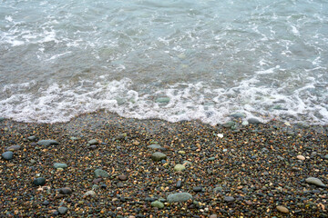 Sea waves wash over a pebble beach made of natural rounded gravel