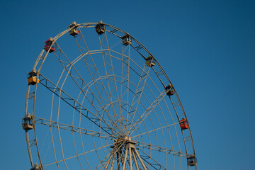 Ferris wheel without people in the clear blue sky. Ferris wheel in the park in bright sunlight during the day. Large white circular construction. Rides and attractions for children