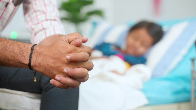 Rack focus shot, Close up shot of father hands praying for daughters health recovery at hospital near bed - concept medical treatment, parenthood and togetherness