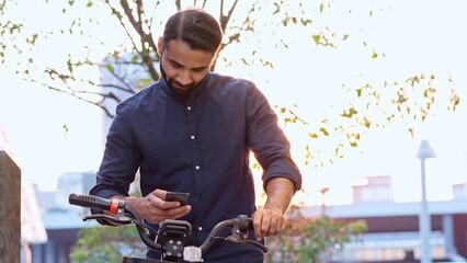 Indian business man holding smartphone using bike rental digital phone app scanning qr code to rent electric bicycle in city public eco transport mobile application standing on urban park on sunset. - Powered by Adobe