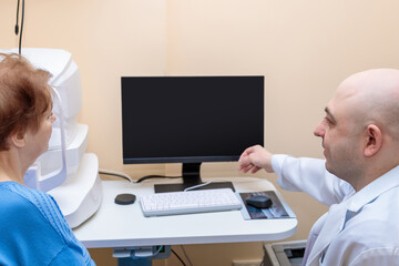 A male ophthalmologist explains the results of an eye examination to an adult woman, showing a...