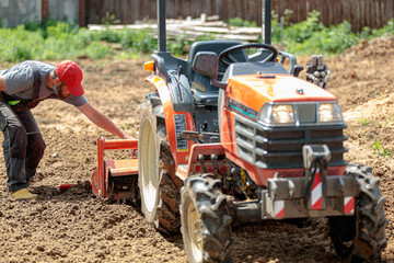 A man on a mini-excavator levels a piece of land, loosens the soil