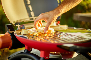 Fototapeta Close up on man's hand put bread, roasting bruschetta on the barbecue gas grill outdoor in the backyard, Breakfast On Grill, summer family picnic, food on the nature. obraz