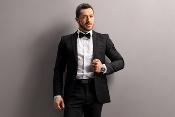 Male model in a black suit and bow tie leaning on a wall