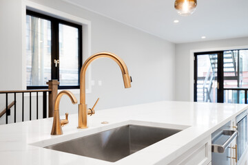 A gold kitchen faucet detail shot with an all white kitchen, a gold light hanging from the ceiling...