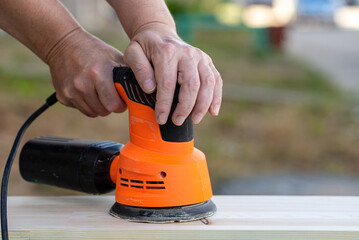 A carpenter is grinding a wooden part with an electric sander. Joiner's grinders, furniture manufacturing.