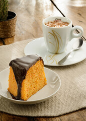 Delicious piece of carrot cake with chocolate cover and a cup of hot cocoa on an afternoon table set