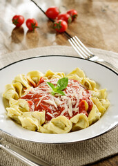 Homemade capeletti or capellini with tomato sauce, basil and grated cheese on a wood table set