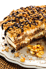 Appetizing ice cream cake with peanuts crumble and chocolate drizzle, missing a piece, on an antique plate, white background